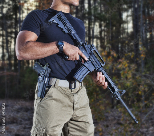 Ready for anything with a handgun by his side and assault rifle in hand in a dark forest