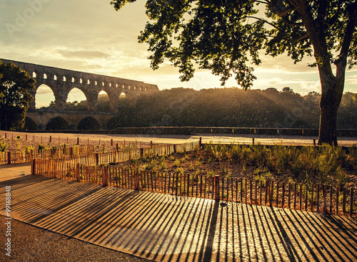 Sun shines through falling raindrops while setting down at Pond du Gard - Roman aqueduct, France.