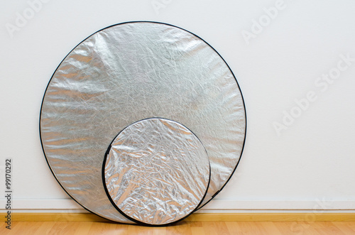two round silver reflectors against the white wall of a photo studio