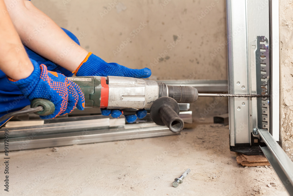 Garage doors installation. Worker drills a hole for the bolt Garage doors installation. Worker drills a hole for the bolt