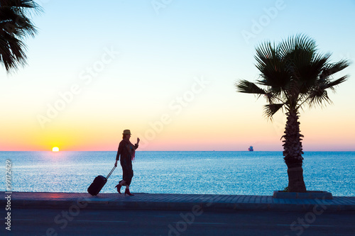 Exotic Vacation Silhouette of Female pulling Travel Suitcase on Seafront