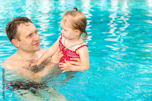 Fotografie Active father teaching his toddler daughter to swim in pool on tropical resort