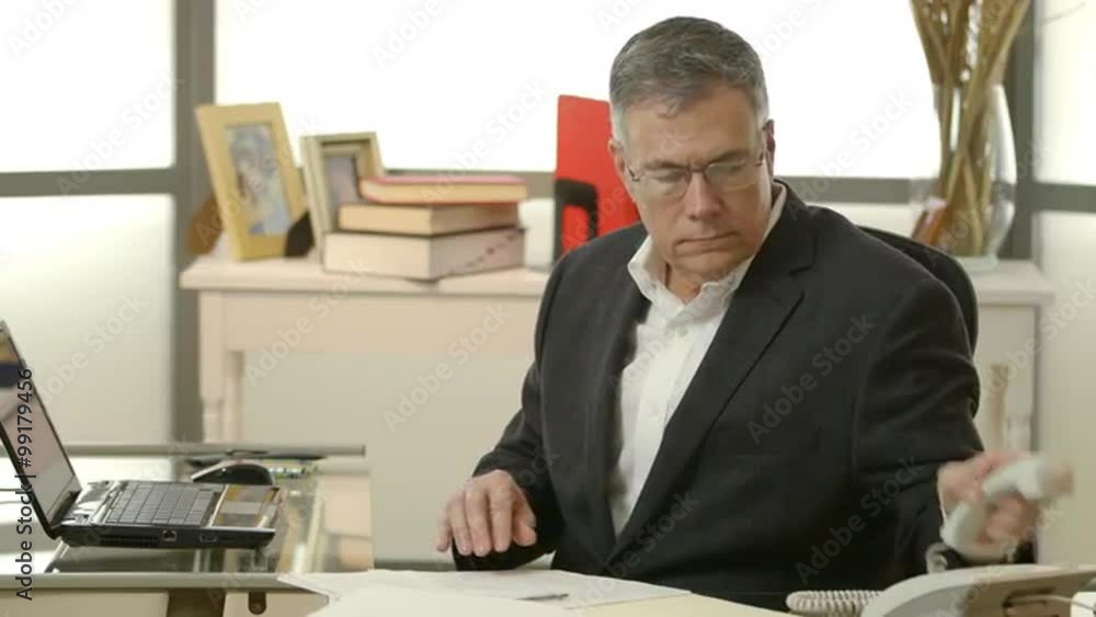 businessman sitting at his office desk takes a phone call businessman sitting at his office desk takes a phone call