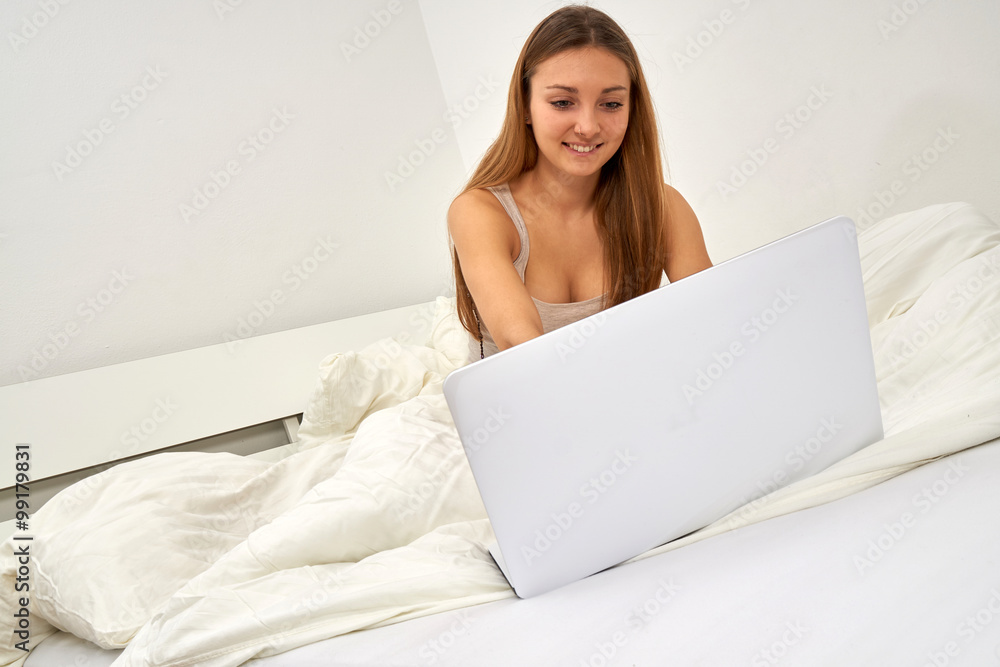 Junge Frau sitzt auf ihrem Bett und nutzt ihren Laptop Junge Frau sitzt auf ihrem Bett und nutzt ihren Laptop