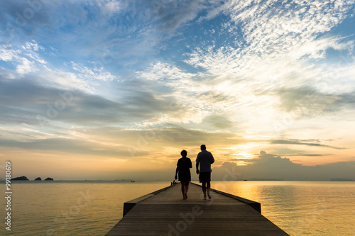 Elderly couple walking on the pier at sunset on a tropical island