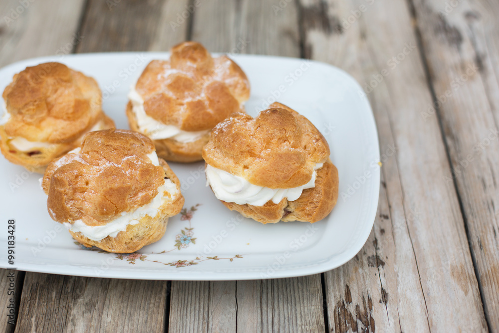 four big homemade profiteroles with cream on wooden table - perfect summer desert four big homemade profiteroles with cream on wooden table - perfect summer desert