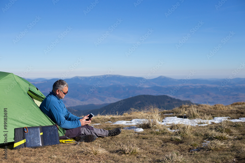 The solar panel attached to the tent. The man sitting next to mobile phone charges from the sun. The solar panel attached to the tent. The man sitting next to mobile phone charges from the sun.