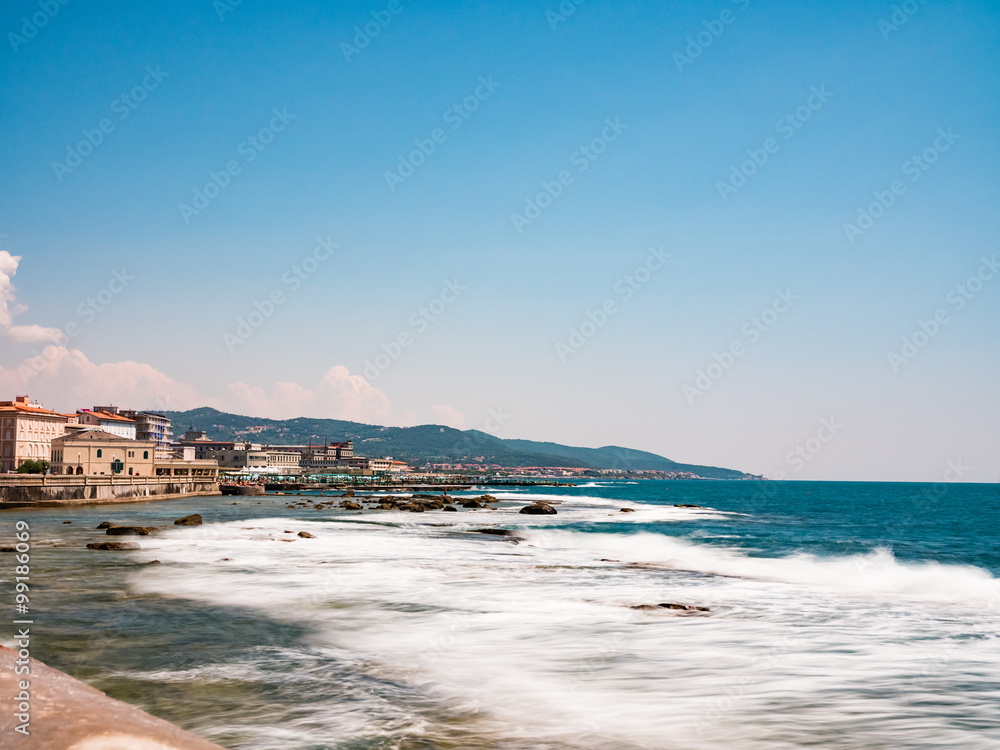 A sunny day view of Livorno on the Italian westcoast in Tuscany. Taken from the beachwalk along the ocean. You look south over the hills and waves are coming in from the sea.
