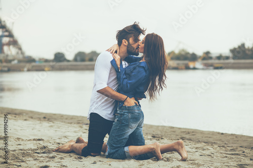 Young couple kissing on the sand by the river