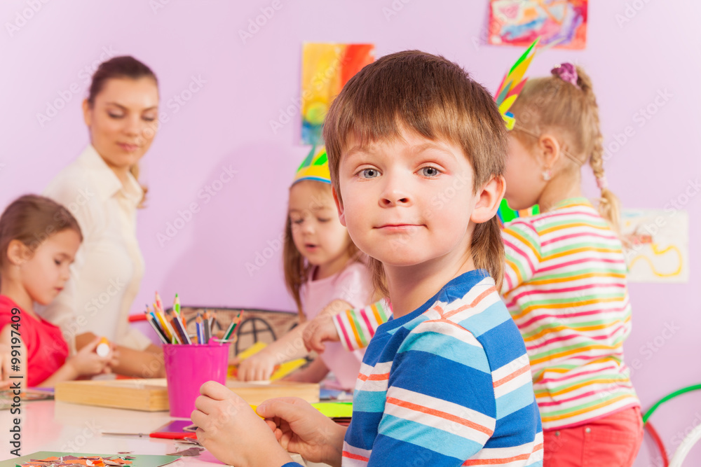 Boy by the table in kindergarten class with mates Boy by the table in kindergarten class with mates