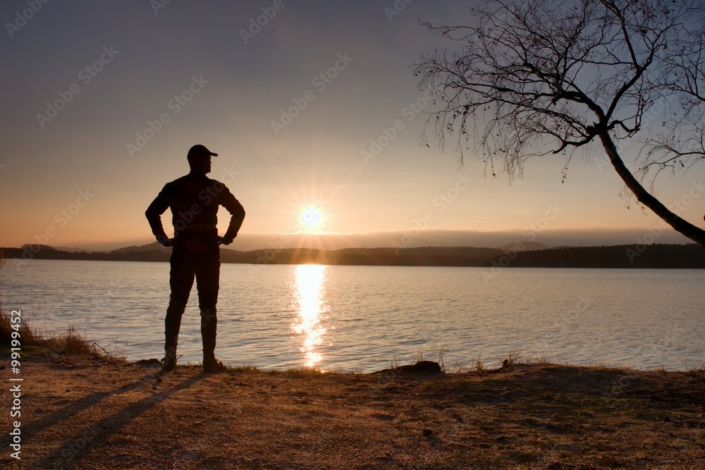 Lone sportsman looking at colorful  sunset on shore of autumn lake