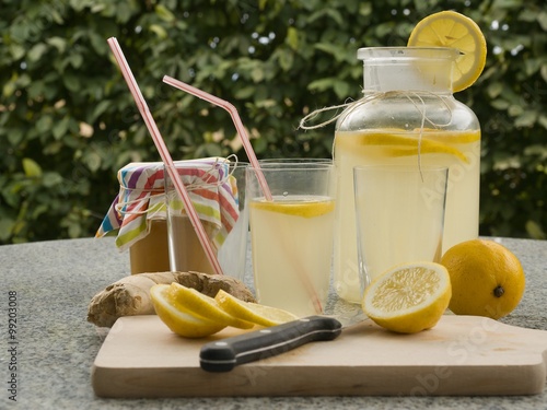 Detailed Picture of all ingredients neccesary to cook a homemade lemonade consist from water, lemon, ginger and glass of honey. Pitcher, chopping board, kitchen knife, lemon slices, glasses with straw photo