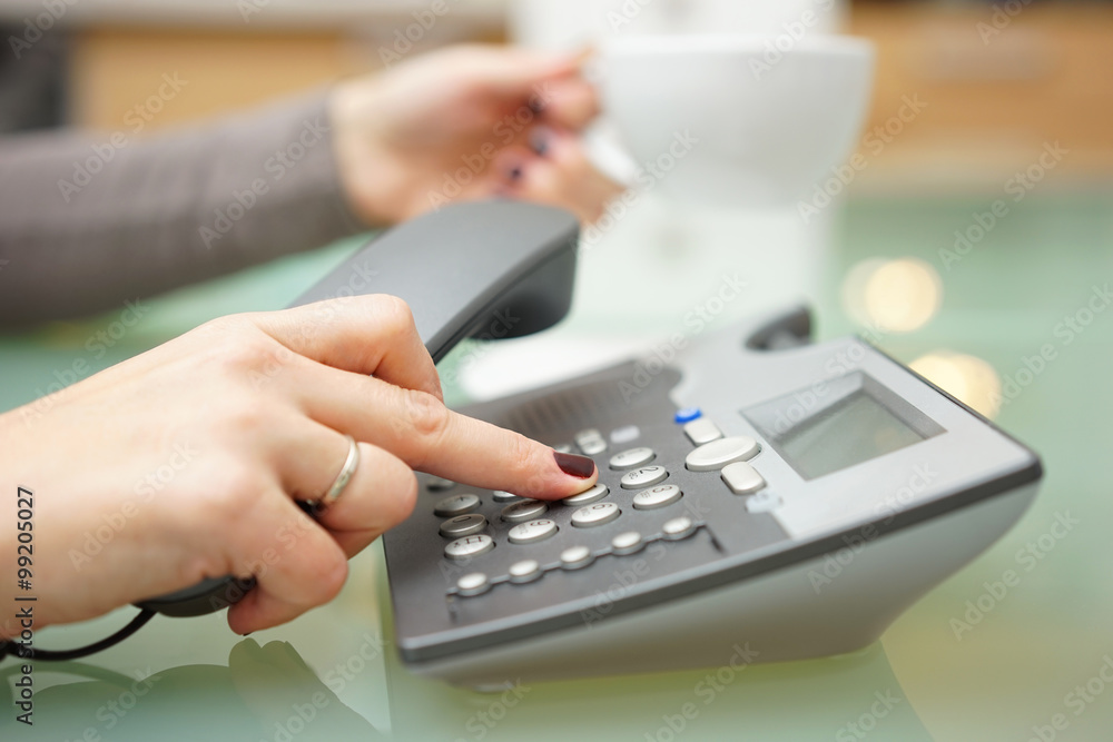Woman is pressing button on on the phone dial pad and drinking c Woman is pressing button on on the phone dial pad and drinking c