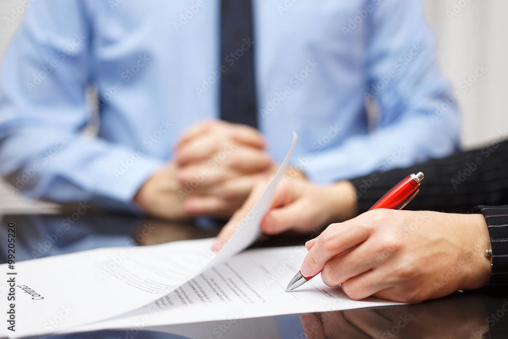 woman is signing contract with business man in background - obrazy, fototapety, plakaty 