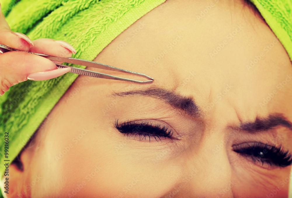 Beautiful woman plucking her eyebrow. foto de Stock Adobe Stock