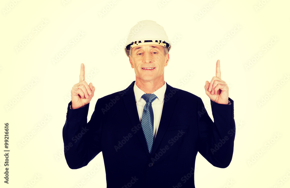 Smiling businessman with hard hat pointing up Smiling businessman with hard hat pointing up