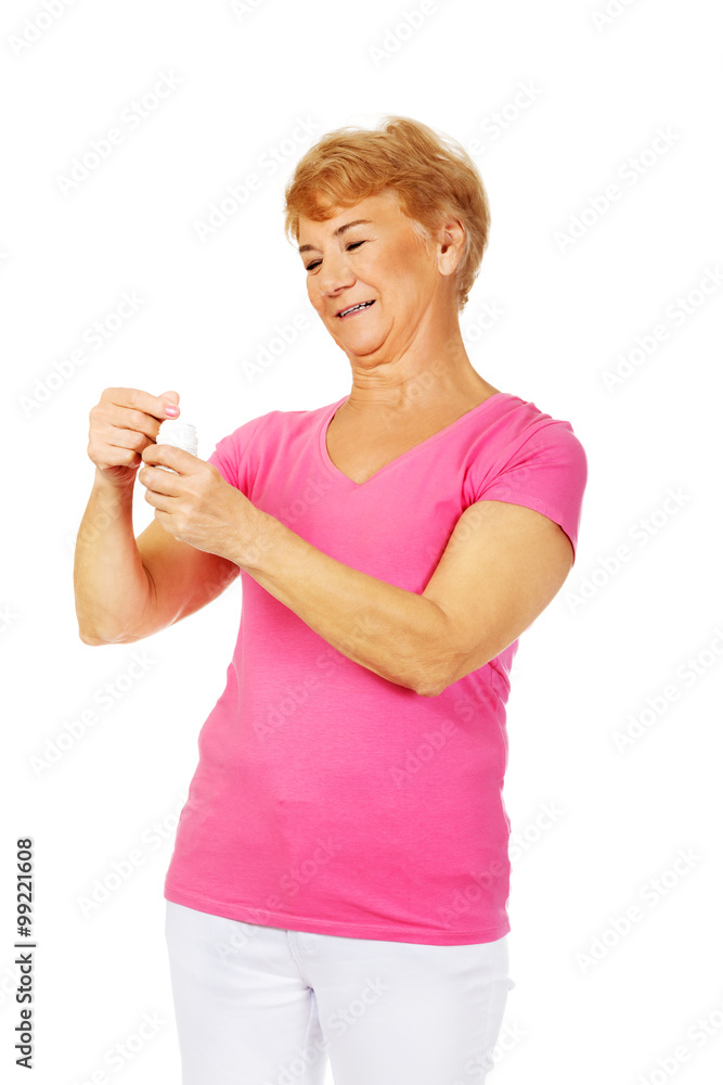Obraz premium Smiling senior woman holding jar of pills