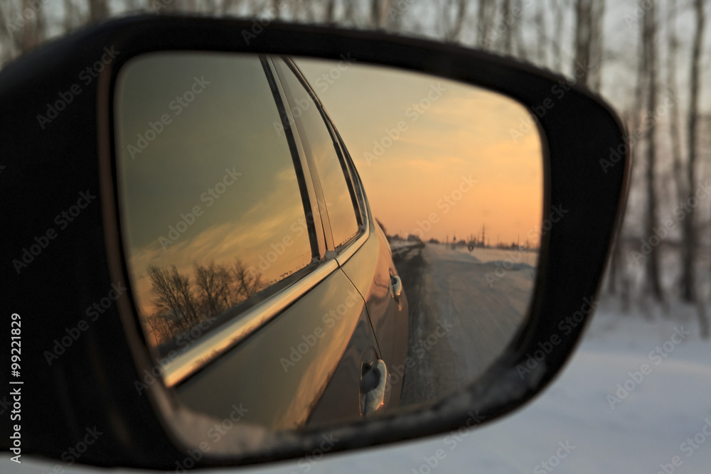 Reflection winter road in the mirror of car at sunset.