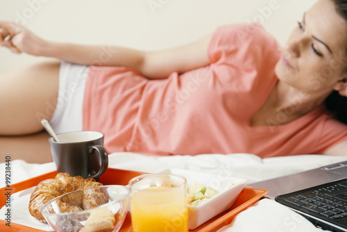 Woman resting on bed and having breakfast.