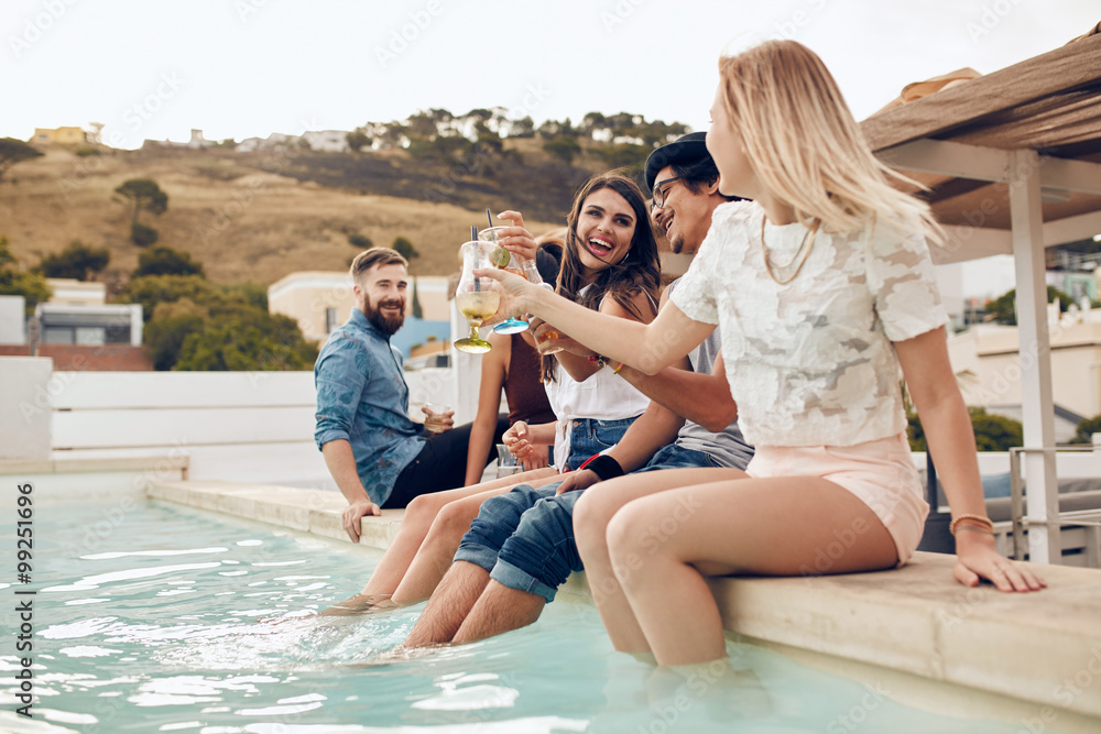 Friends partying by the pool toasting cocktails