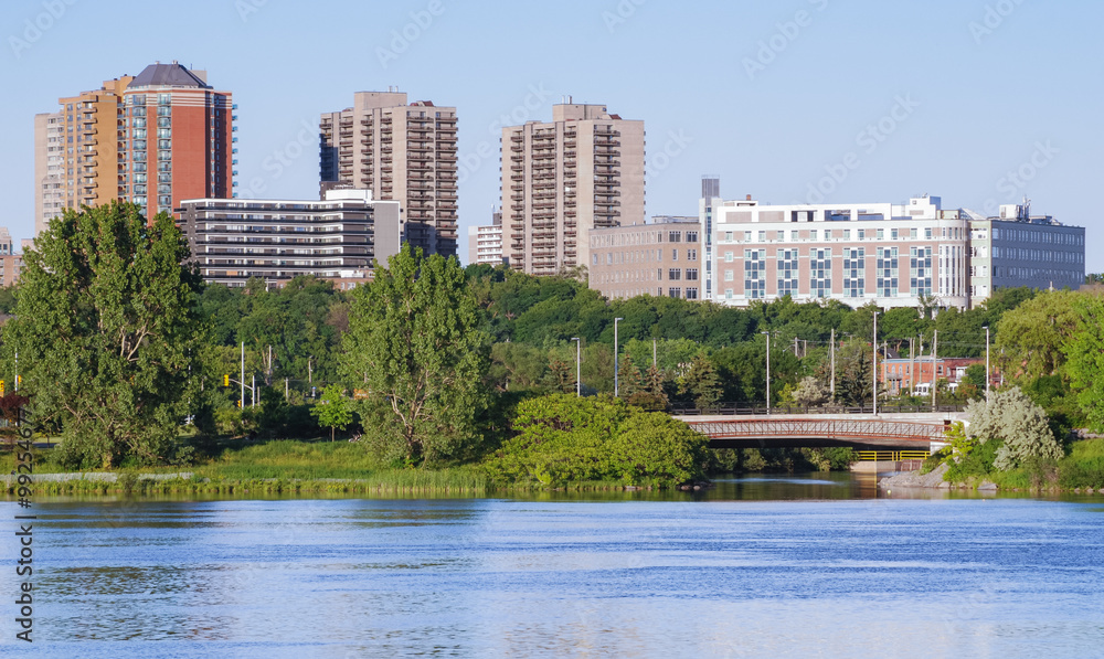 Ottawa River and capitol city skyline along the parkway - late springtime afternoon - early evening approaches.  Tall buildings, apartments and condominiums comprise an Ottawa city skyline.