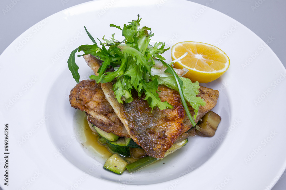 Cooked dorado fish with vegetables and lemon in white plate Cooked dorado fish with vegetables and lemon in white plate