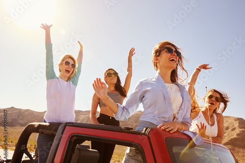 Four Female Friends On Road Trip Standing In Convertible Car