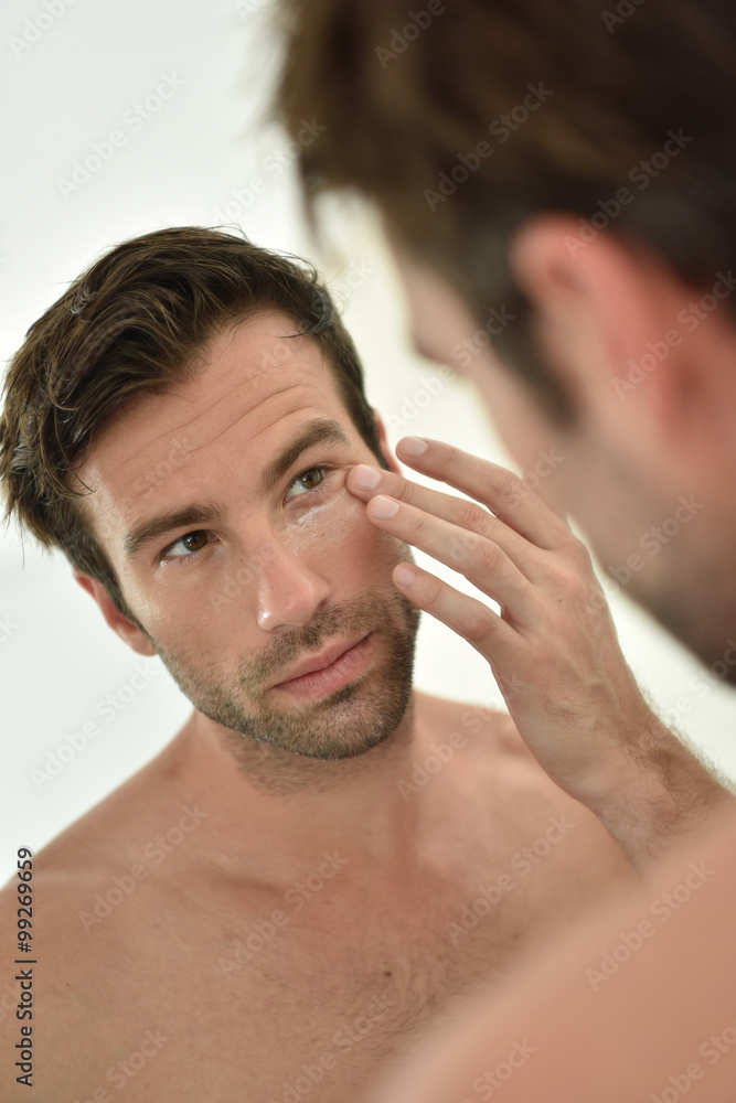 Obraz premium Handsome man applying facial cream in front of mirror