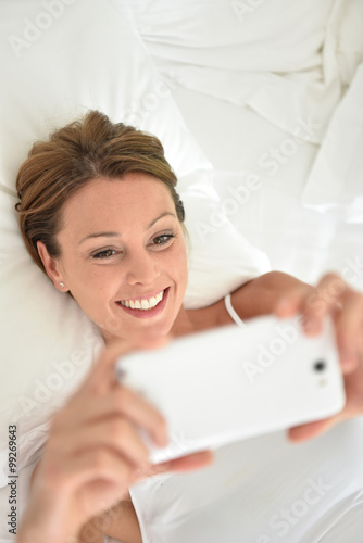 Woman laying on bed and using smartphone
