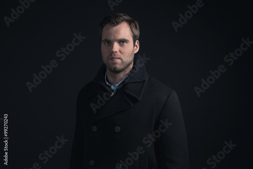 Stubbly bearded young man wearing dark blue winter coat.