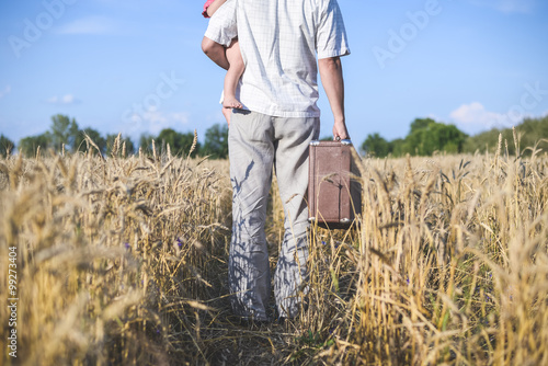Backview of father holding baby and walking in wheat field