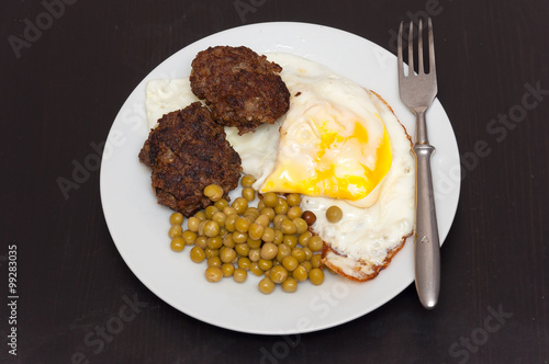 Scrambled eggs, meat and green peas in white plate