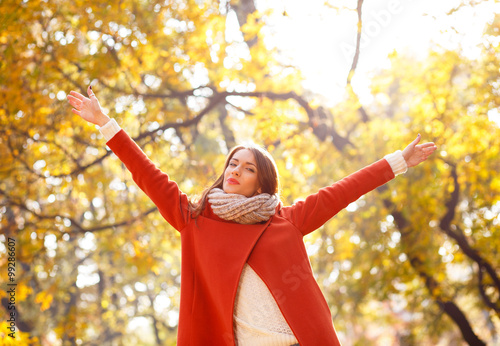 Portrait of a young woman in a park with arms outstretched.