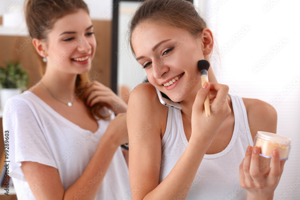 Beautiful girls looking in the mirror and applying cosmetic with a big brush Beautiful girls looking in the mirror and applying cosmetic with a big brush