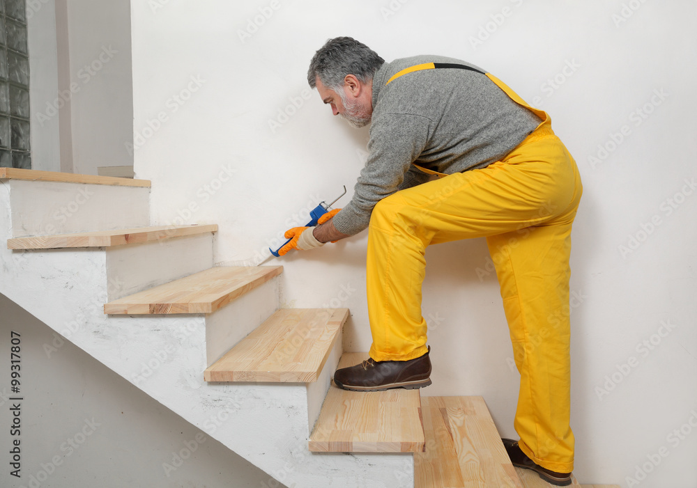 Home renovation, worker caulking wooden stairs with silicone
