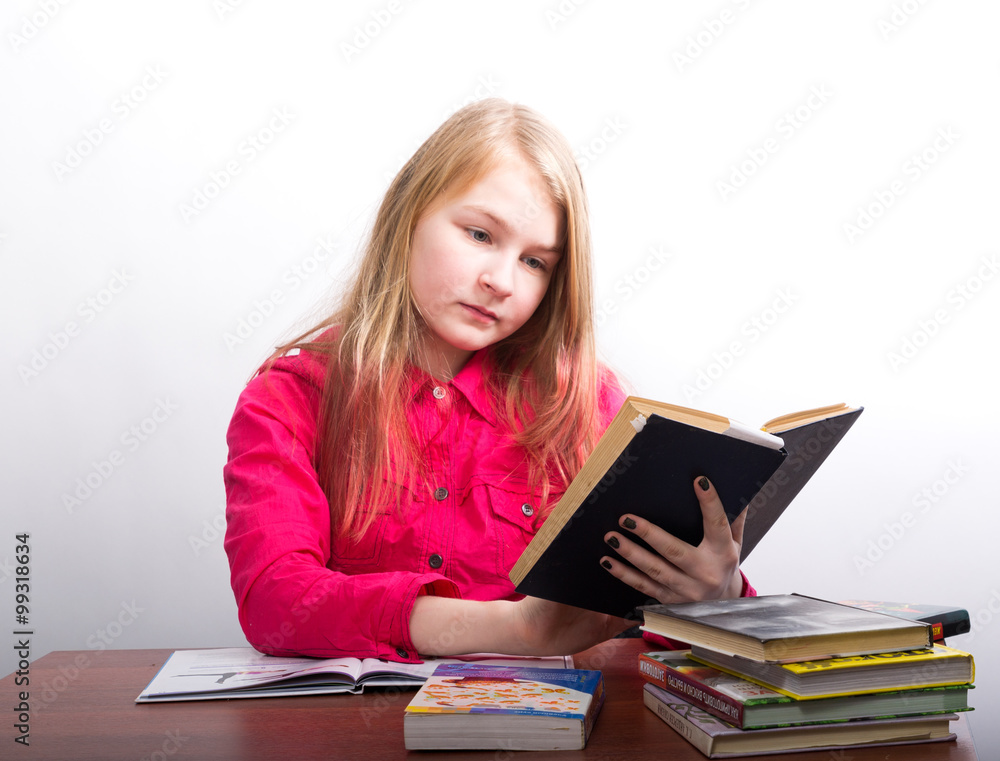 teenager girl sitting at a table in front of her large pile of books. schoolgirl reading a book and doing homework