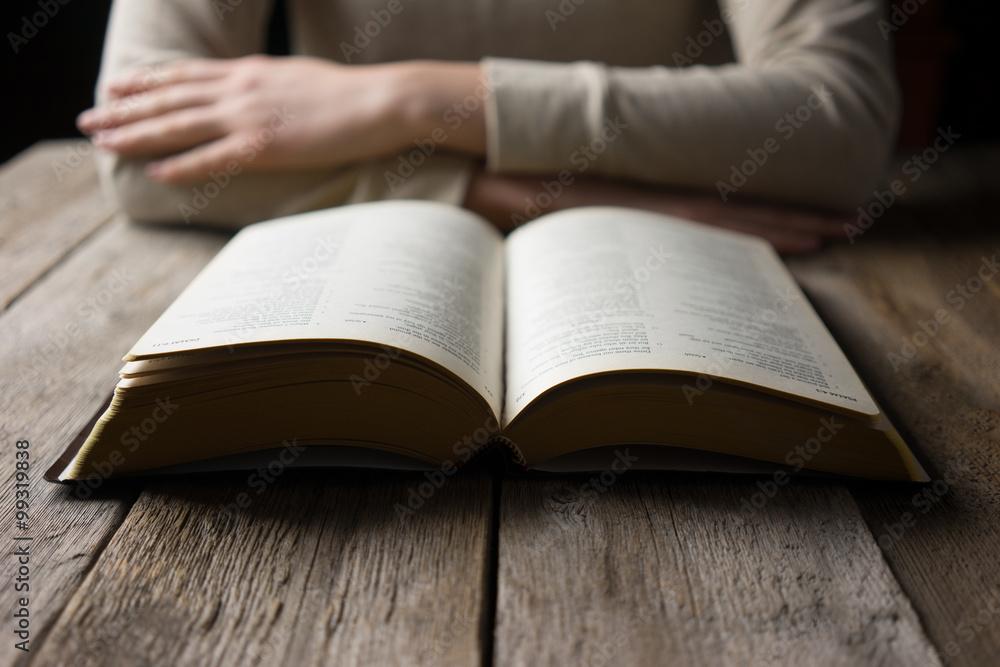 woman reading the bible in the darkness over wooden table woman reading the bible in the darkness over wooden table