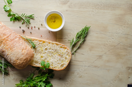 Sliced bread ciabatta watered with extra virgin olive oil with herbs  on wooden background. View from above.