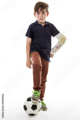 Full length shot of a young boy who cant play football with his friends because he has broken his left arm photo