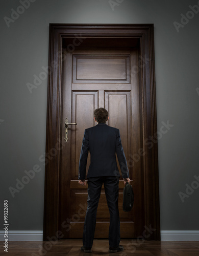 Small young businessman standing in front of the huge door
