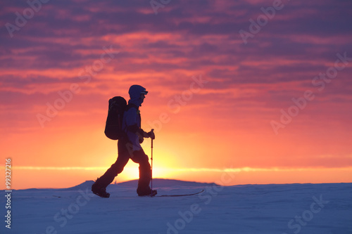 Alone skier walking mountains against sunset