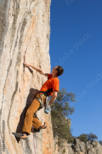 Young male climber hanging by a cliff.