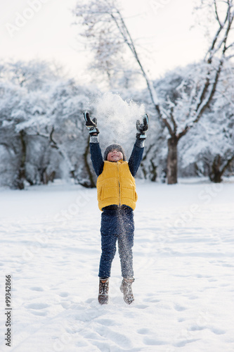 boy jumping throwing snow up near the forest