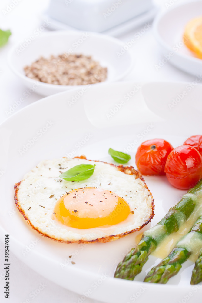 Fried egg with asparagus and tomatoes on a white plate with blue napkin. closeup..