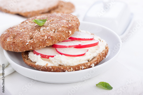 Sandwich with wholewheat bread, cottage cheese, radish and basil on a white plate, closeup, selective focus.