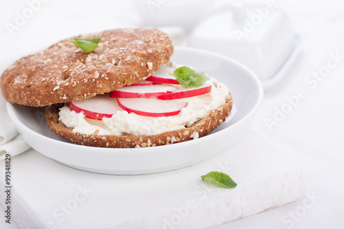 Sandwich with wholewheat bread, cottage cheese, radish and basil on a white plate, closeup, selective focus..