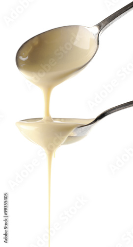 Condensed milk pouring from spoons  isolated on white