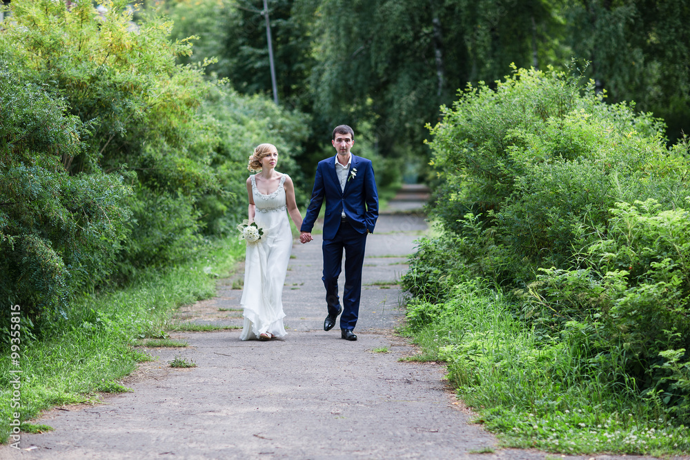 Fototapeta premium A happy young newly married couple walking in the park. Beautiful bride and groom kissing in the woods.