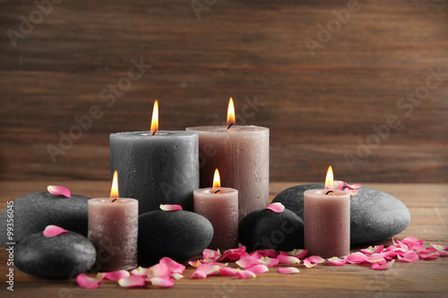 Alight wax grey candle with flower petals and pebbles on wooden background