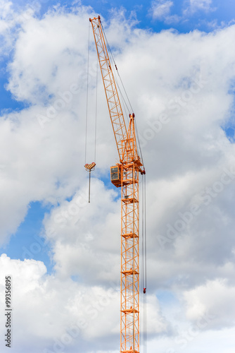 Industrial construction crane against blue sky with clouds
